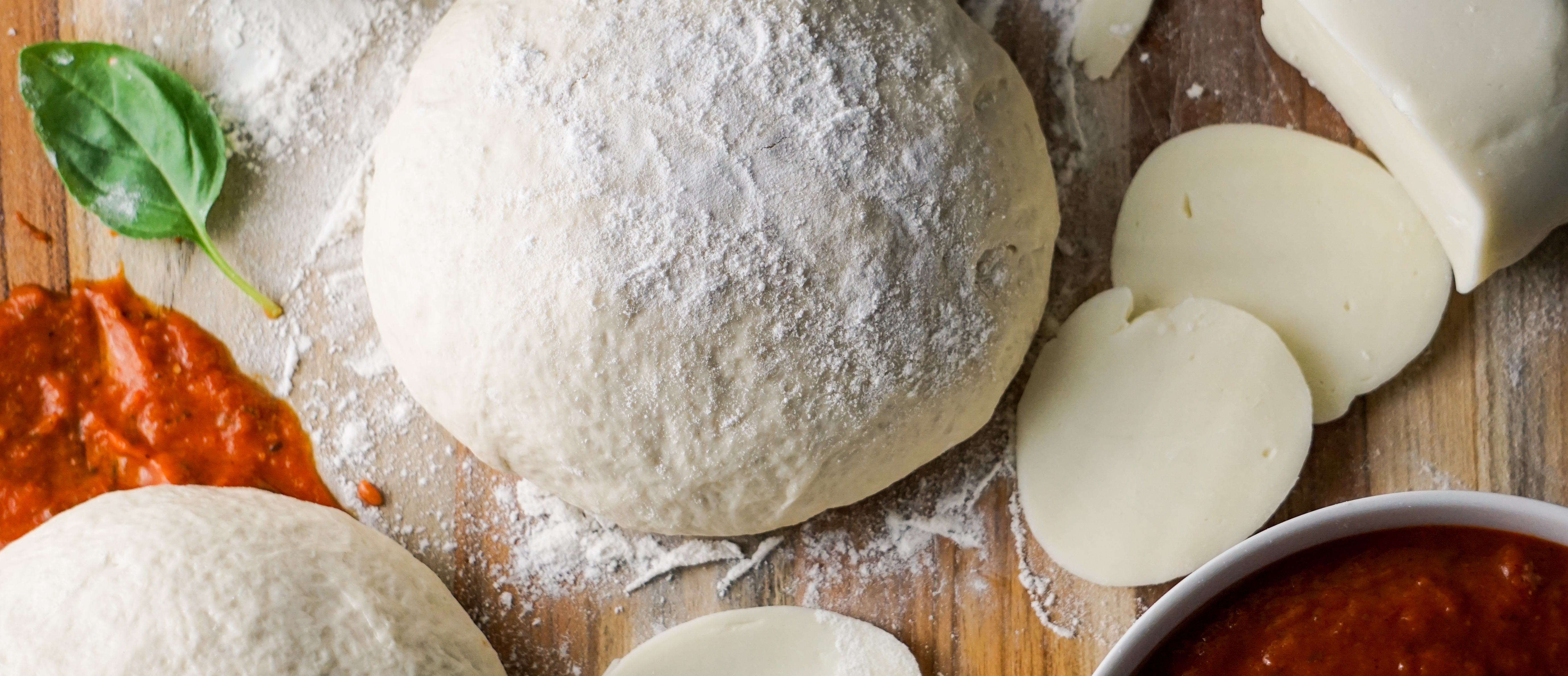 Pizza dough, sauce, mozzarella cheese, olive oil, and basil on a table