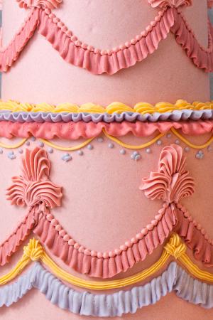 an overpiped 2-tiered cake decorated in pink, yellow, and purple buttercream