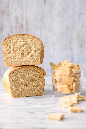 2 stacked halves of beer bread sit next to a cup of beer crackers with several spilled out on a marble surface