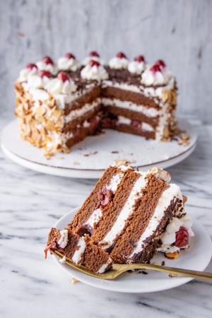 A slice of Black Forest Torte on its side sits on a white plate in front of the remainder of the cake. 