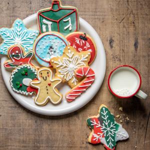 A plateful of sugar cookies decorated for Christmas and Hanukkah with a mug of milk and a cookie with a bite out of it next to it