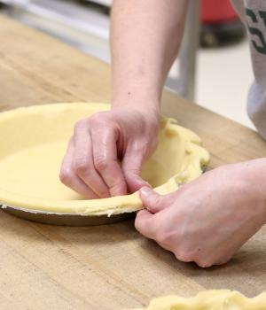 A pair of hands crimping pie dough in a pie pan on a wooden table