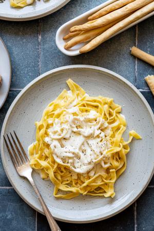 A plate of fettucine alfredo with italian breadsticks on the side