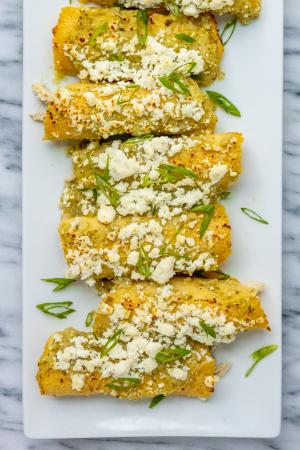 An overhead shot of chicken enchiladas on a white plate topped with cotija cheese and green onions.