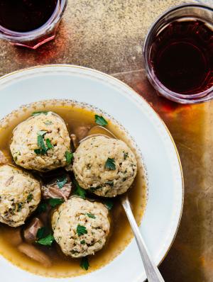 A bowl of matzoh ball soup and 2 glasses of red wine.
