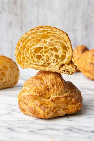 A sliced croissant sits on another croissant with several other croissants around them in the background.