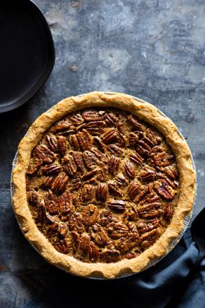 A pecan pie on a mottled metal surface with a dark napkin and a black pie server next to it. 