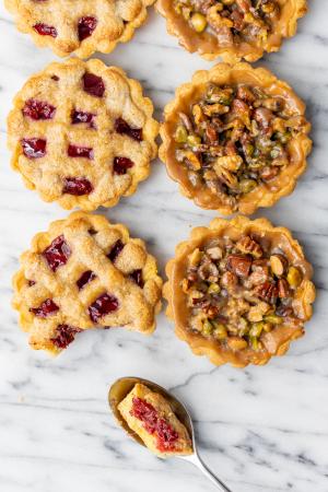 An overhead shot of 6 tarts - 3 cherry almond and 3 caramel nut - with a spoonful taken out of a cherry almond. 