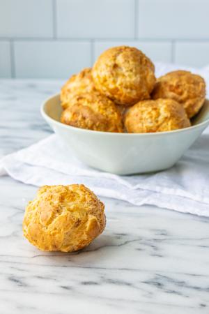 A savory gougeres sits on a marble surface in front of a light mint bowl of more gougeres.