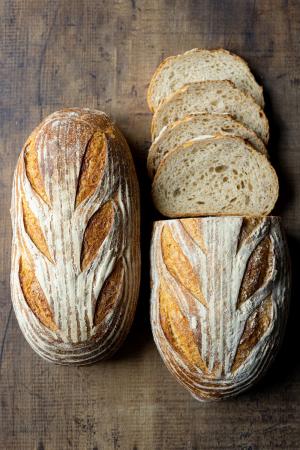 2 loaves of farm bread, one partially sliced on a wooden surface