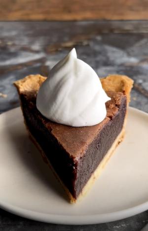 a slice of chocolate chess pie on a small dessert plate with a dollop of whipped cream on top